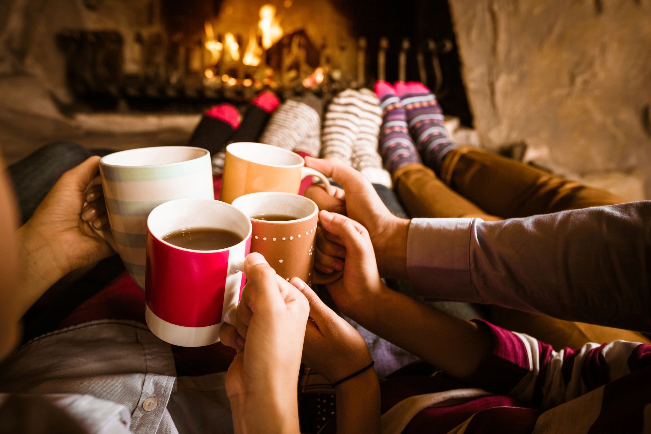 People warming by a fireplace with hot drinks